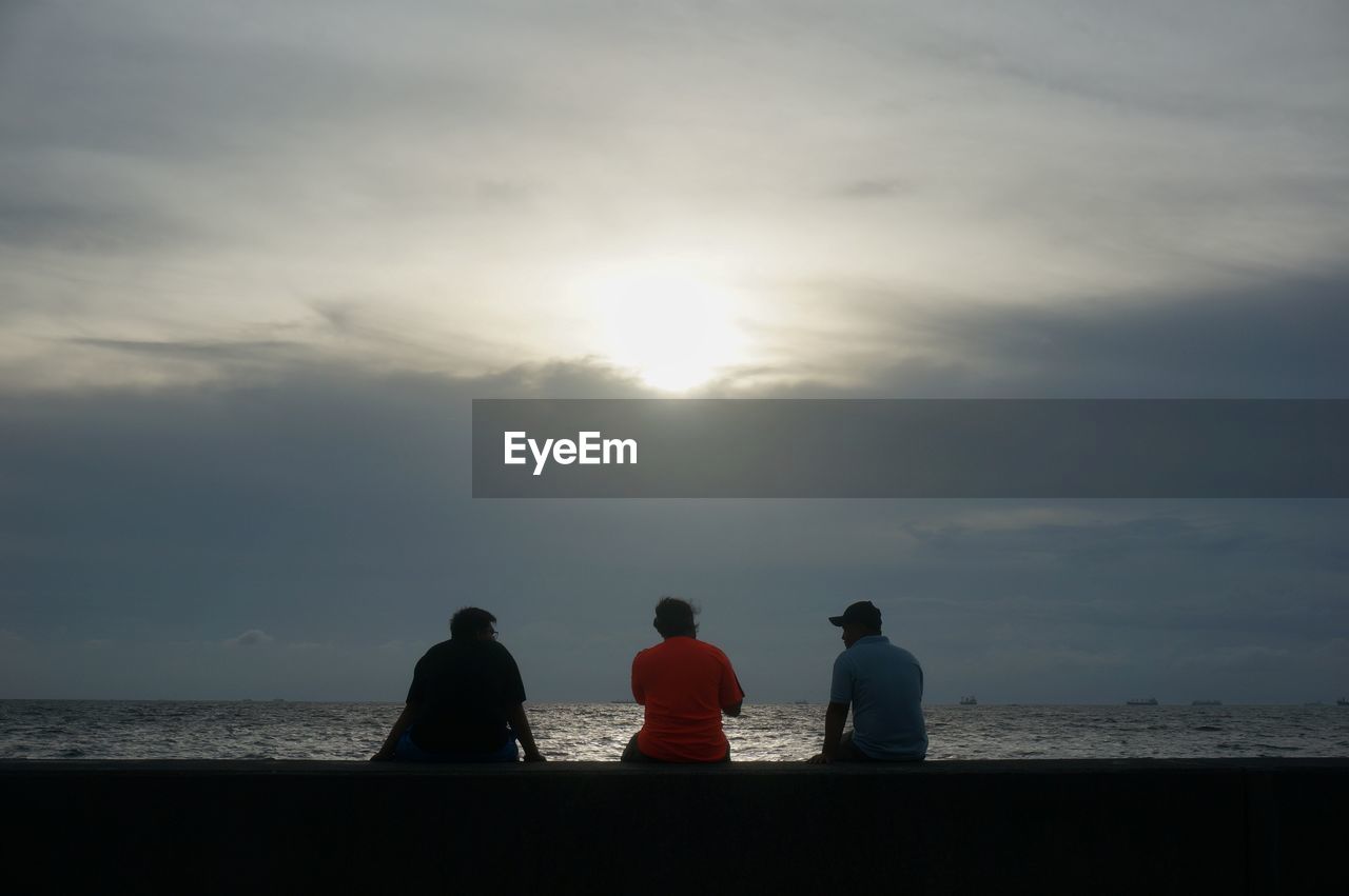 SILHOUETTE OF PEOPLE SITTING ON BEACH