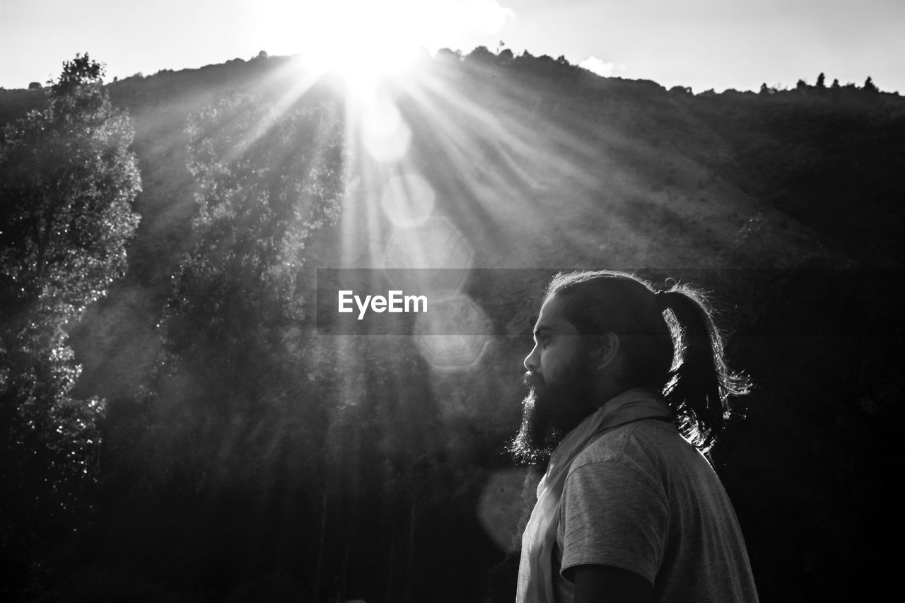 Side view of man standing in forest during sunny day