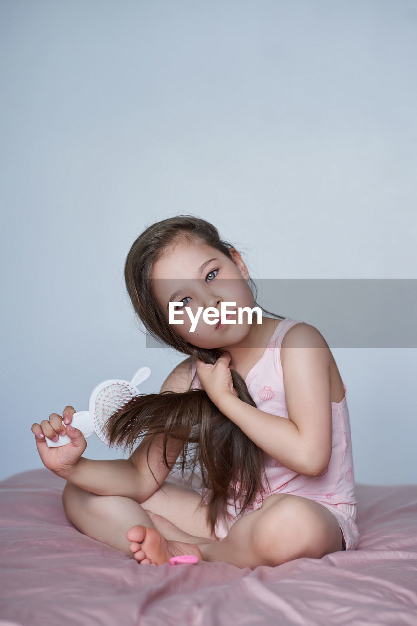 The girl is sitting on the bed and combing her long hair.