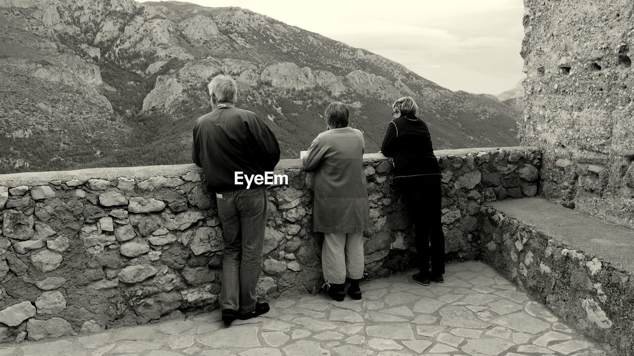 Rear view of man and women standing on fort in front of mountains