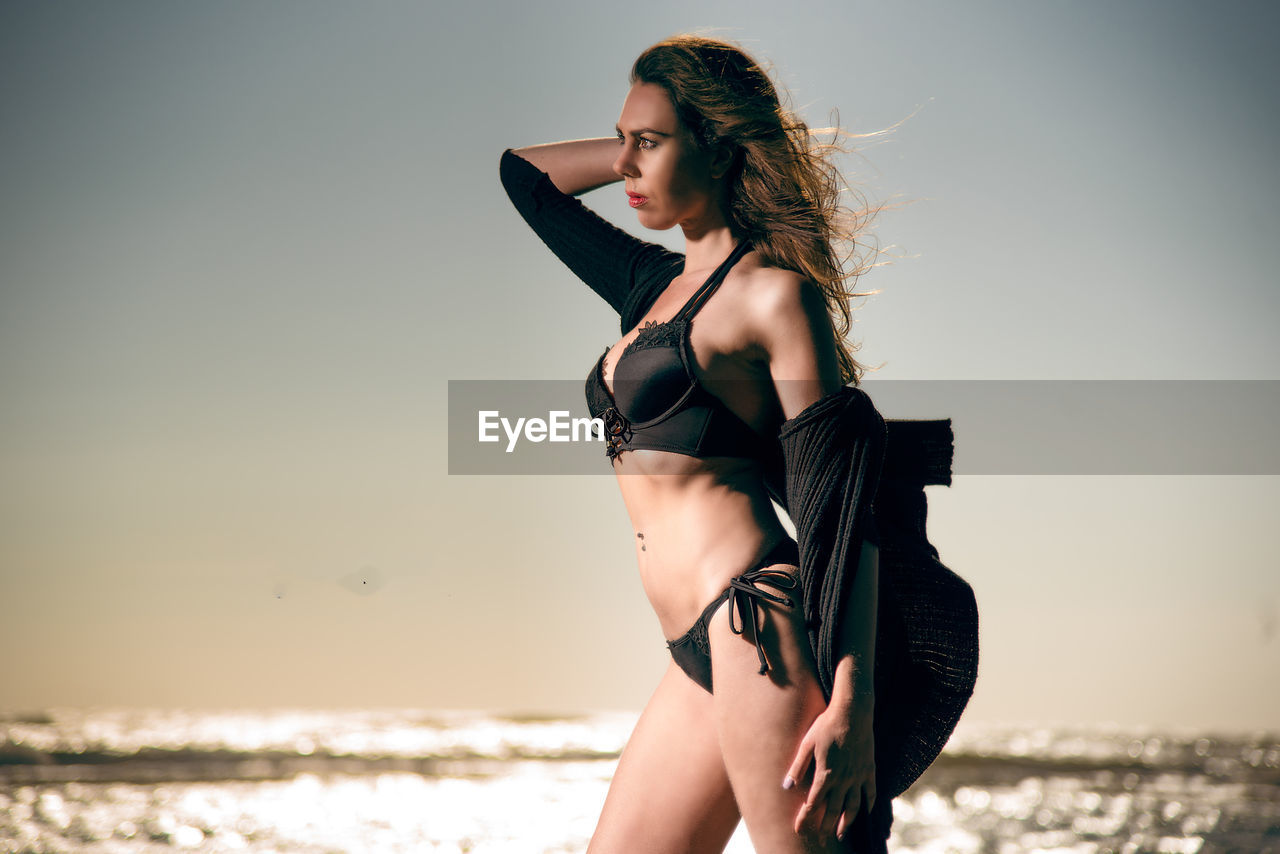 Woman in bikini standing at beach against sky