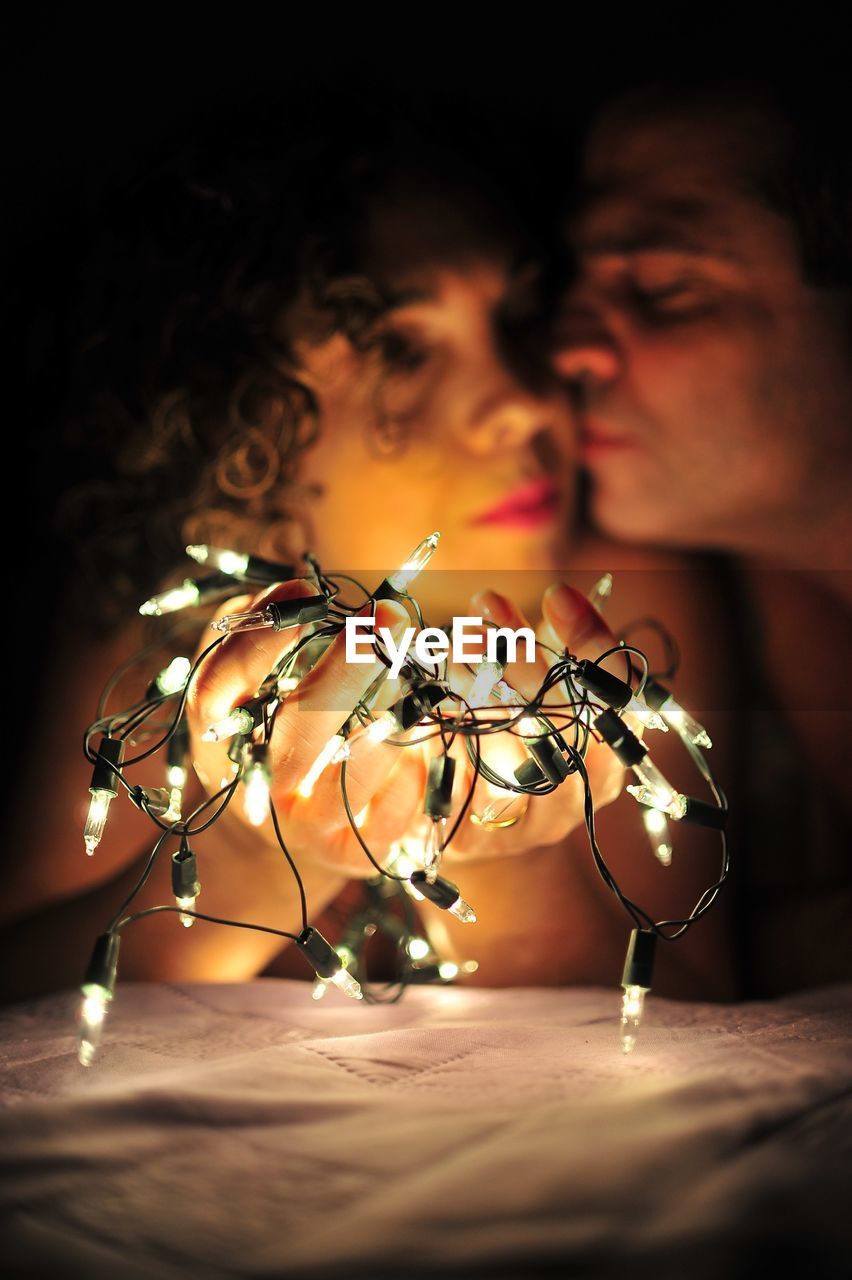 Close-up of illuminated string light against couple in darkroom