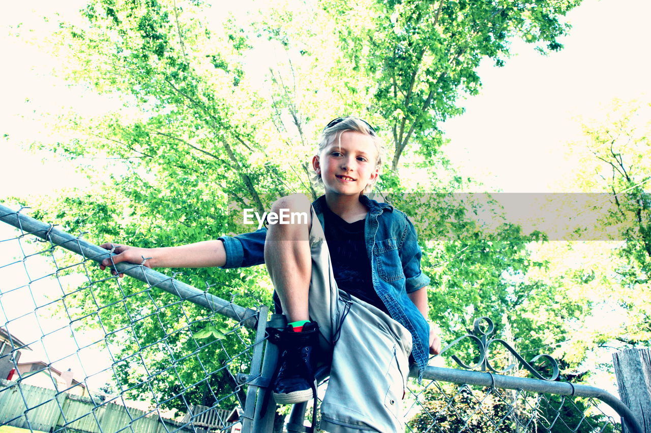 Low angle portrait of boy smiling while sitting on fence