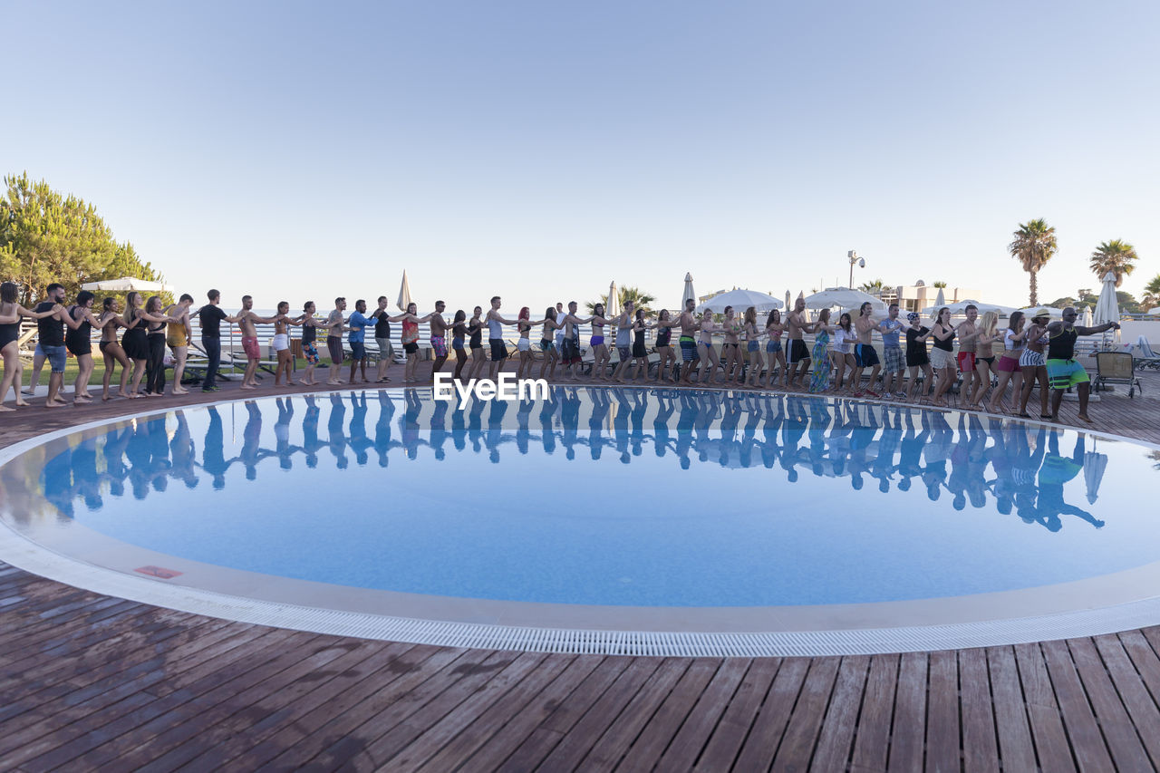 GROUP OF PEOPLE ON SWIMMING POOL AGAINST CLEAR SKY
