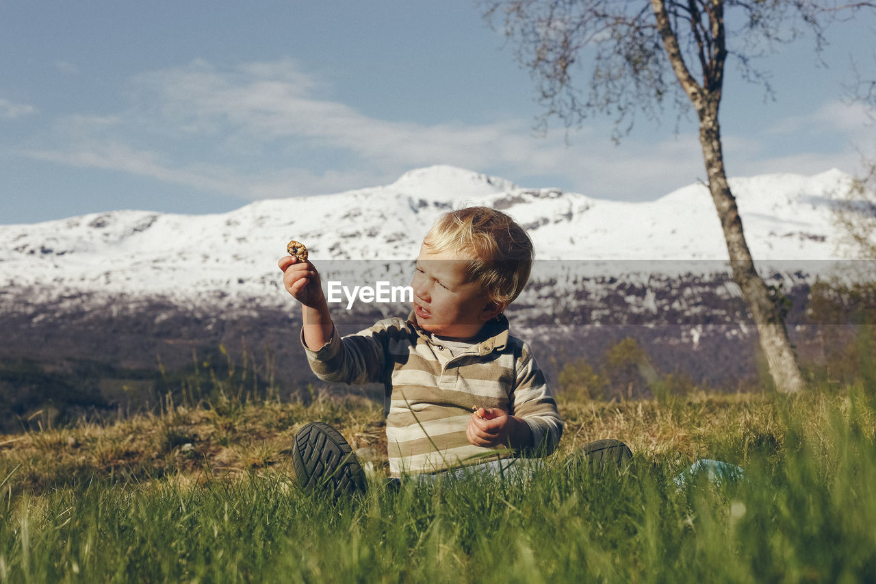 Cute boy holding stone while sitting on grassy land