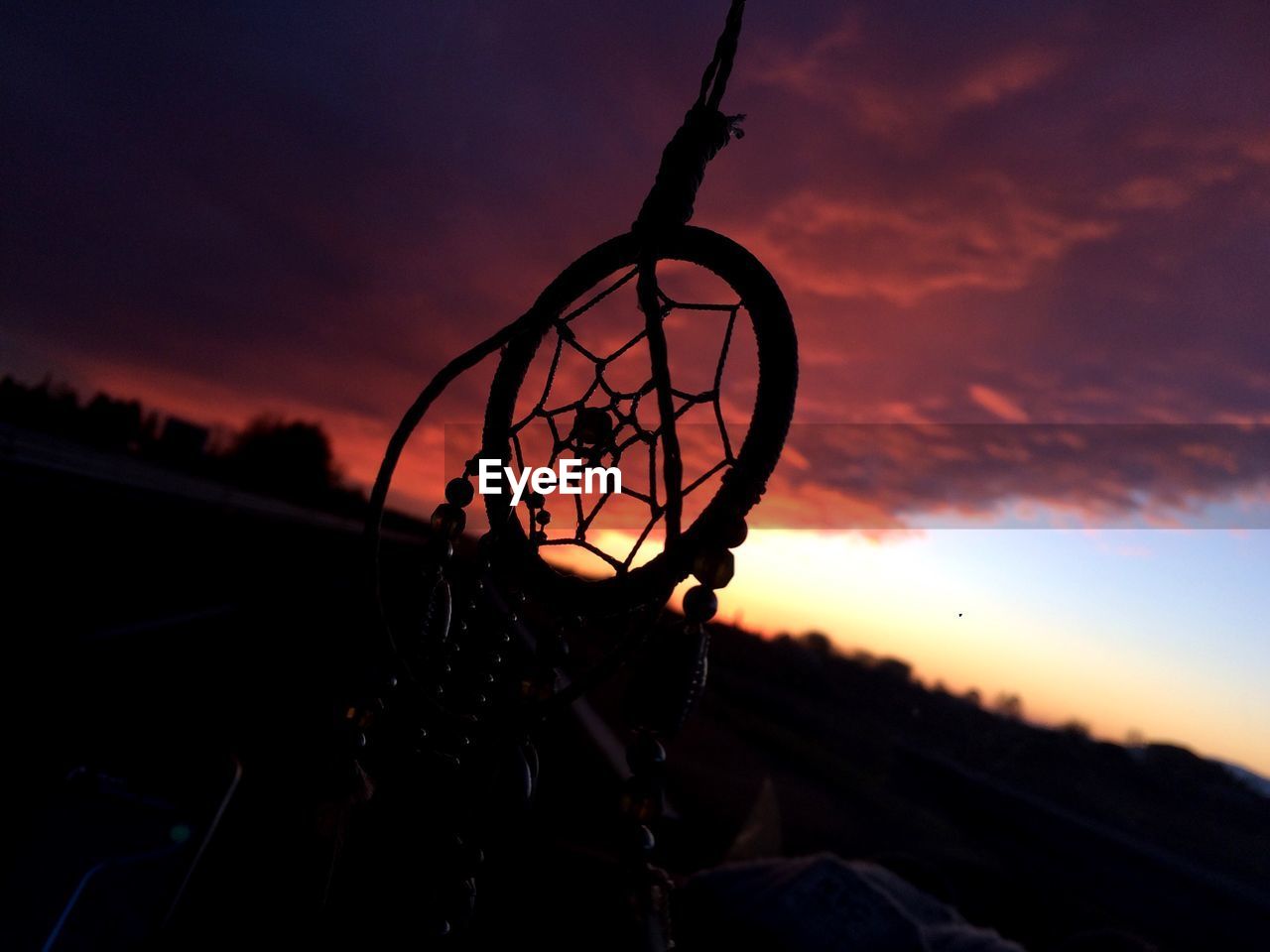 Close-up of silhouette dreamcatcher against cloudy sky at sunset