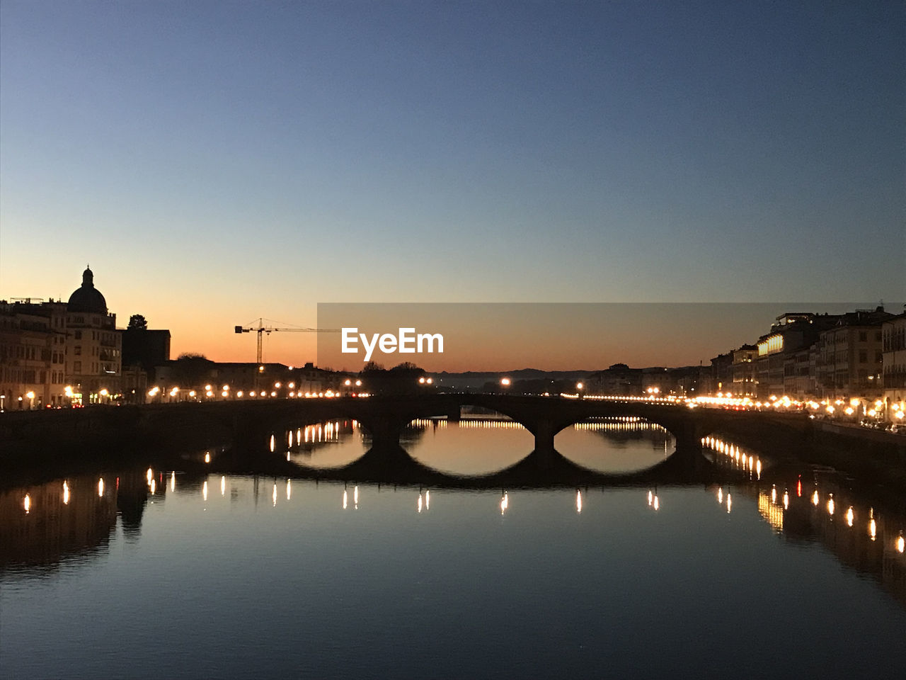 ILLUMINATED BRIDGE OVER RIVER AGAINST SKY IN CITY