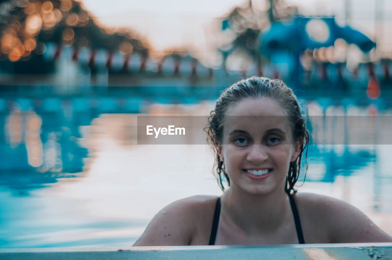 PORTRAIT OF A SMILING YOUNG WOMAN IN SWIMMING POOL