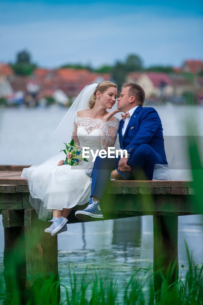 Romantic bride and groom sitting on wooden pier over lake