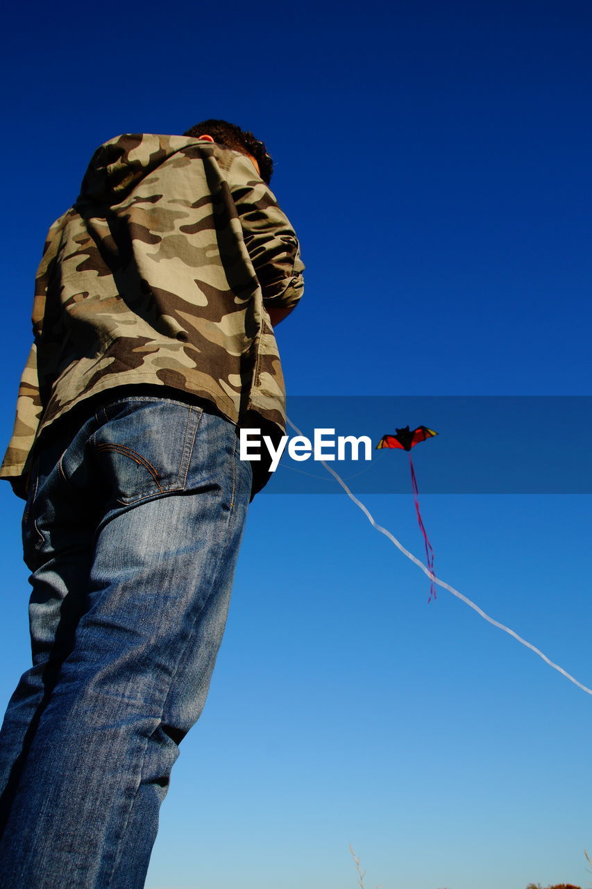 Low angle view of man flying kite against clear blue sky