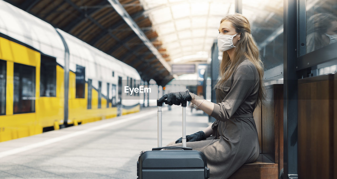 Side view of woman wearing mask sitting at railroad station