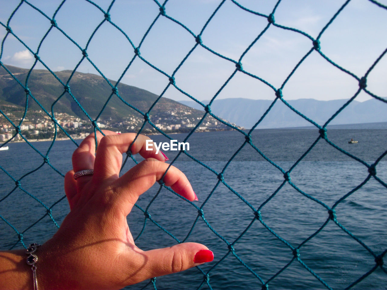 Cropped image of hand holding chainlink ropes against sea 