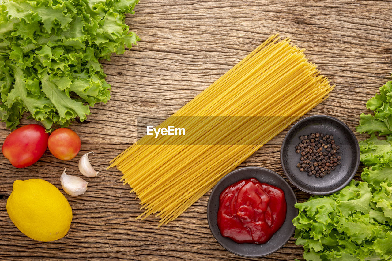 Spaghetti pasta with ketchup, pepper, lettuce, tomato, garlic and lemon on rustic wood, top view