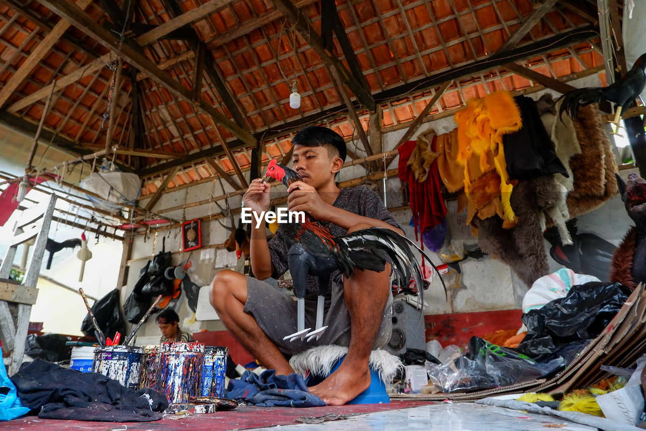 FULL LENGTH OF YOUNG MAN SITTING ON WALL IN SHOPPING MALL