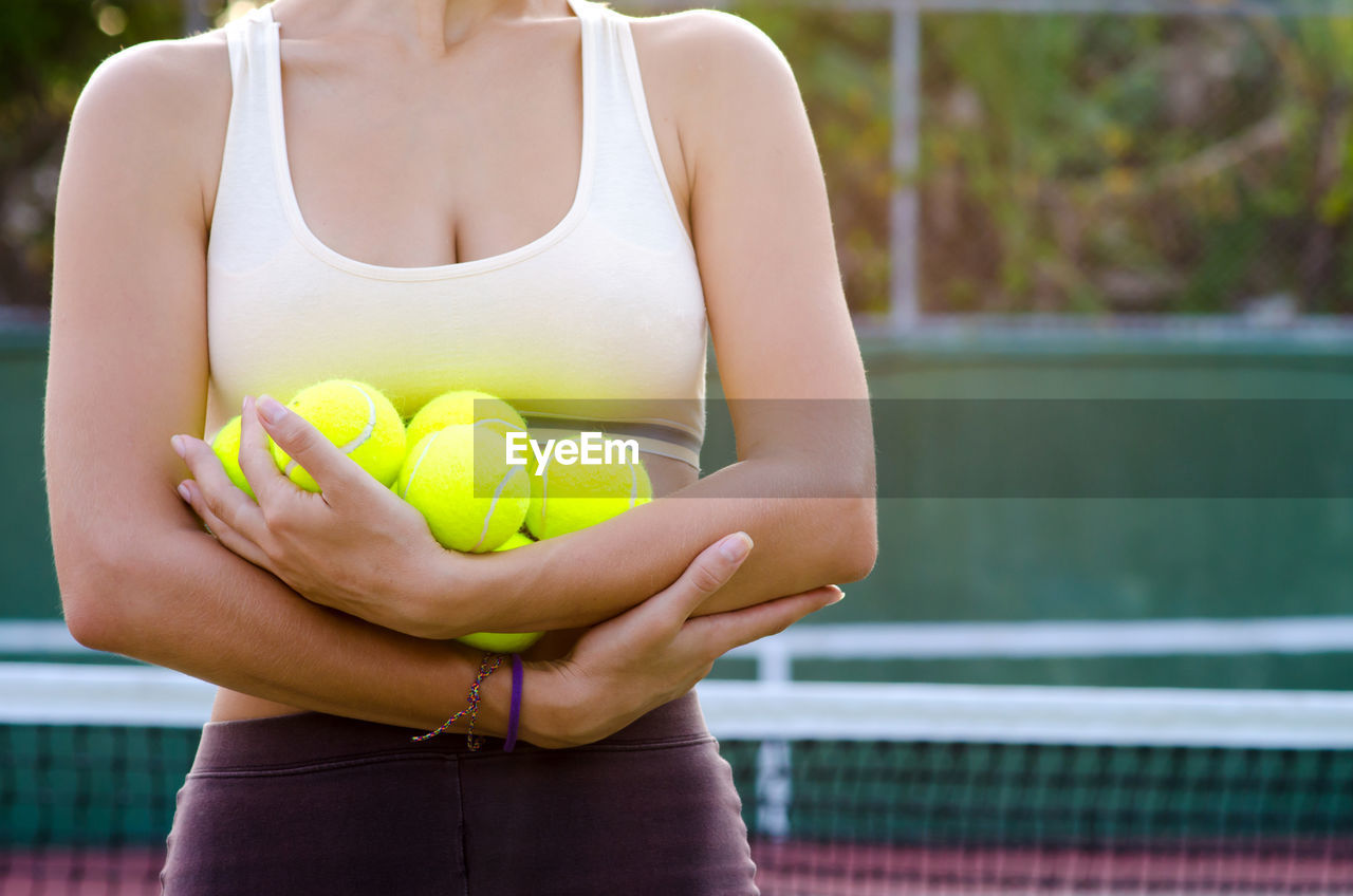 Midsection of woman holding tennis balls while standing in court