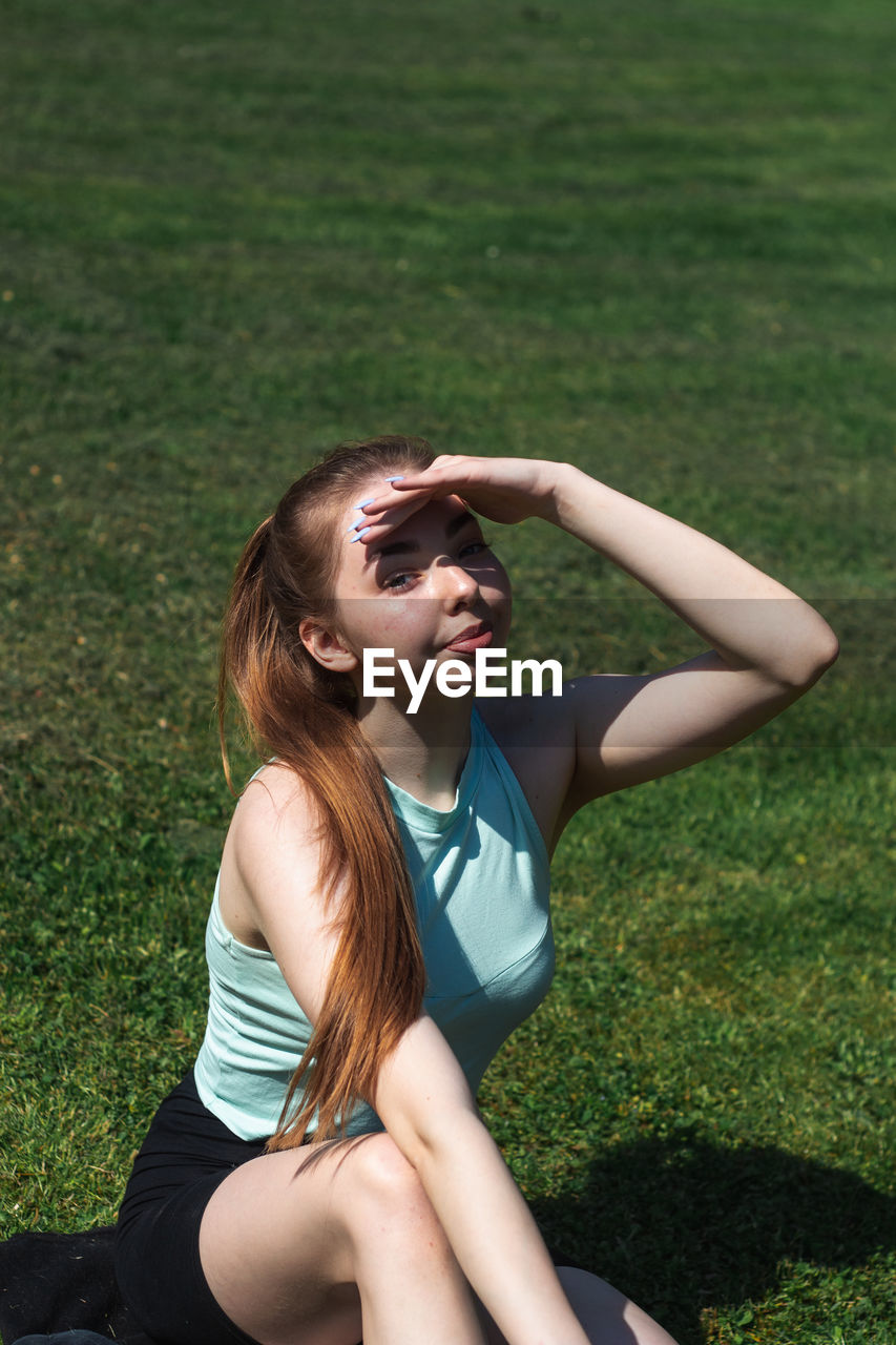 Portrait of woman shielding eyes while sitting in park