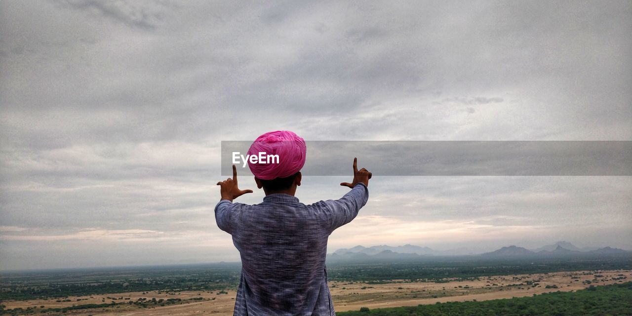 Rear view of man gesturing against sky