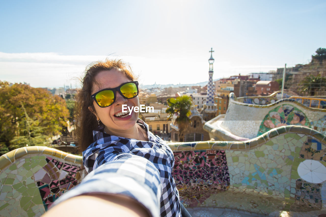 PORTRAIT OF SMILING YOUNG WOMAN WEARING SUNGLASSES AGAINST SKY