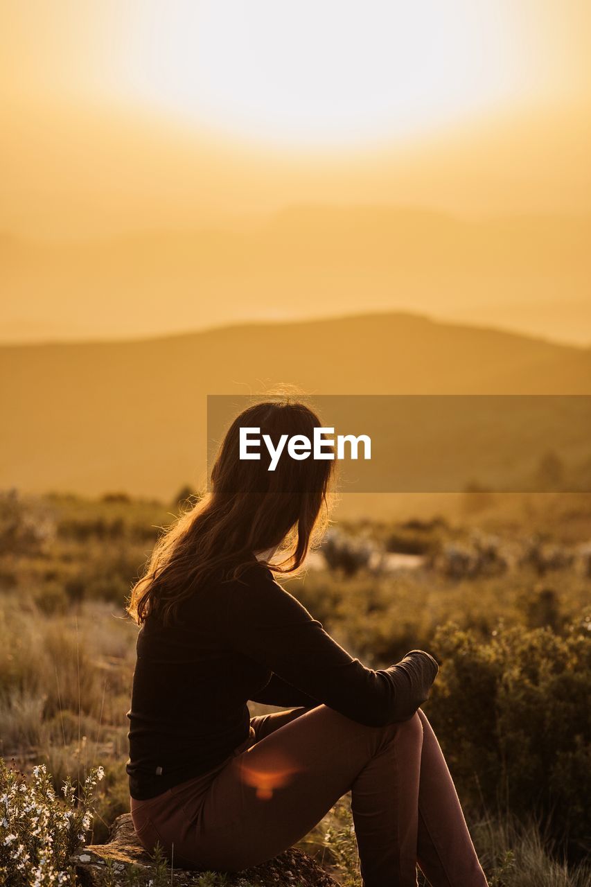 Side view of peaceful female traveler sitting on hill with closed eyes and enjoying nature in highlands at sundown