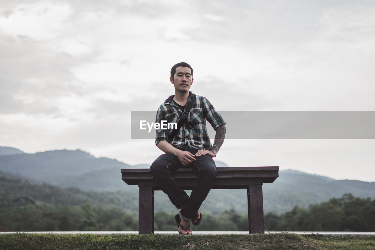 Full length of young man sitting on seat against sky