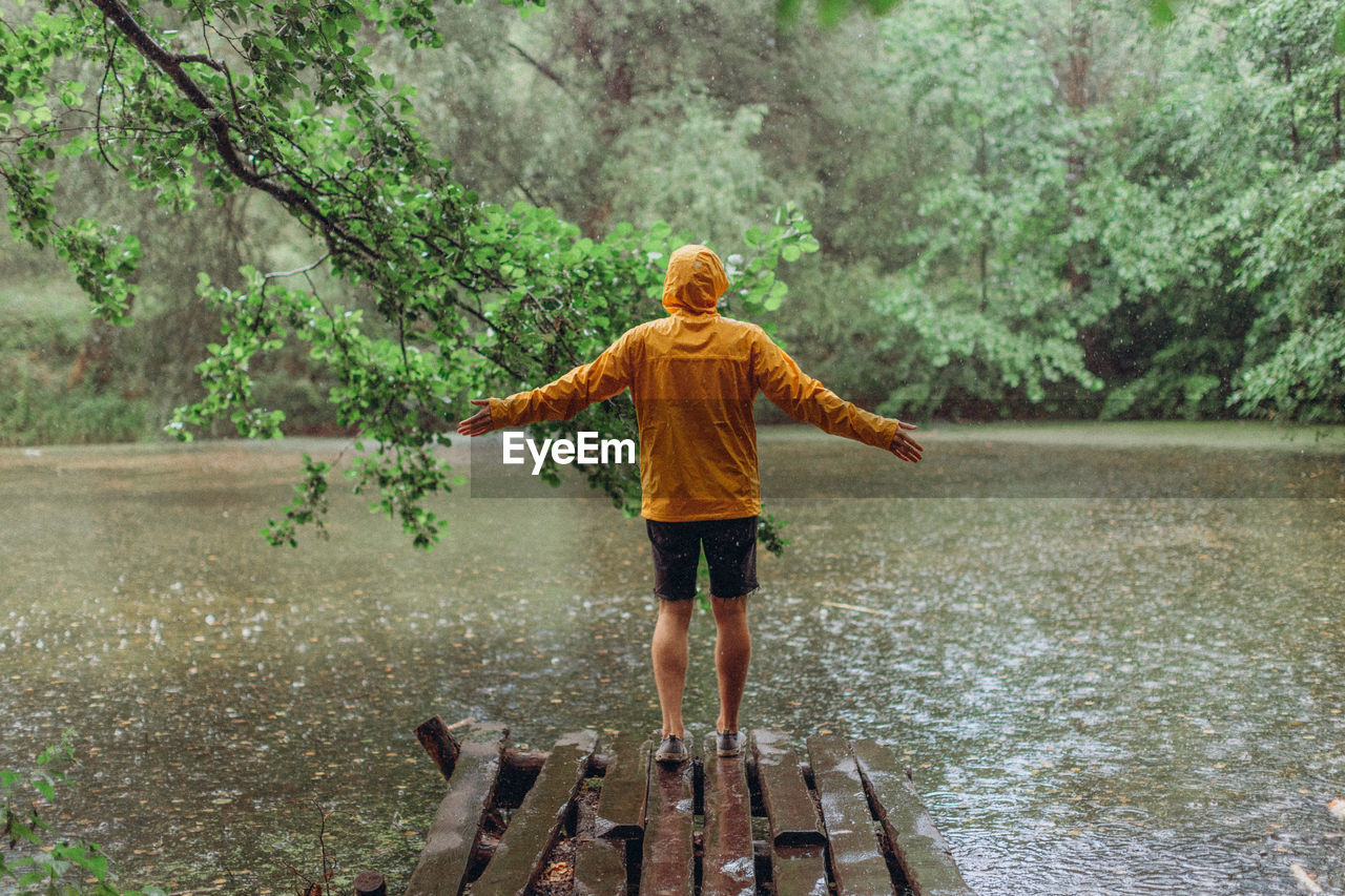 REAR VIEW OF CHILD STANDING ON WATER IN FOREST