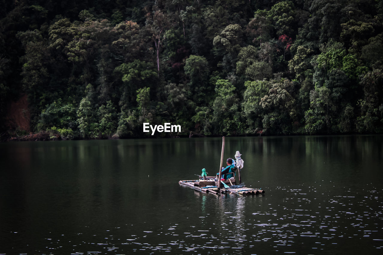 People rowing boat in lake against trees