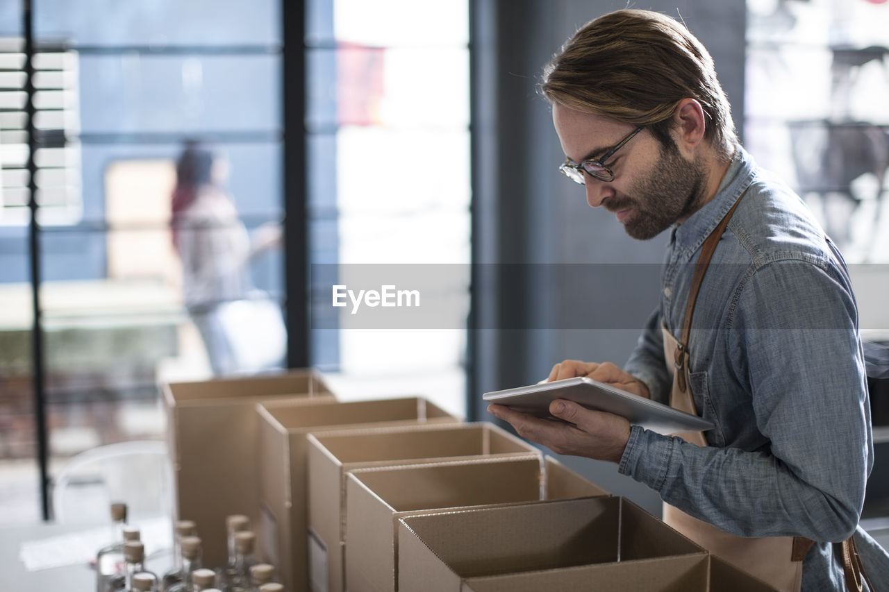 Man surrounded by cardboard boxes using digital tablet