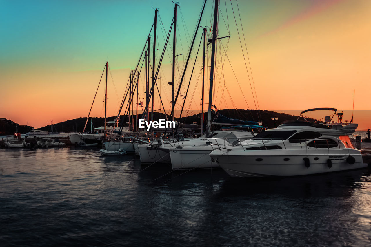 Sailboats moored in harbor at sunset