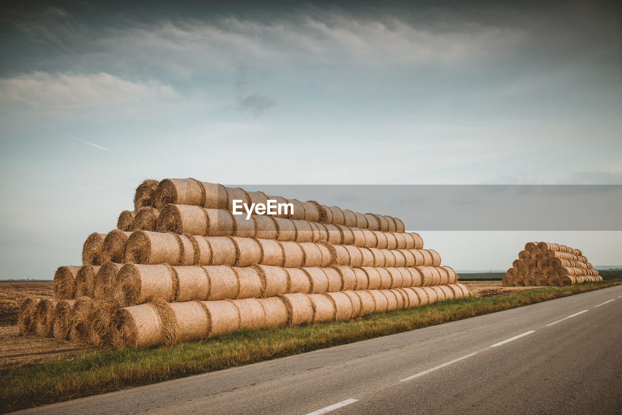 Hay bales on field by road against sky