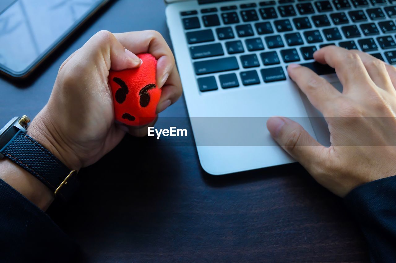 Cropped hand of businessman pressing stress ball while using laptop on table