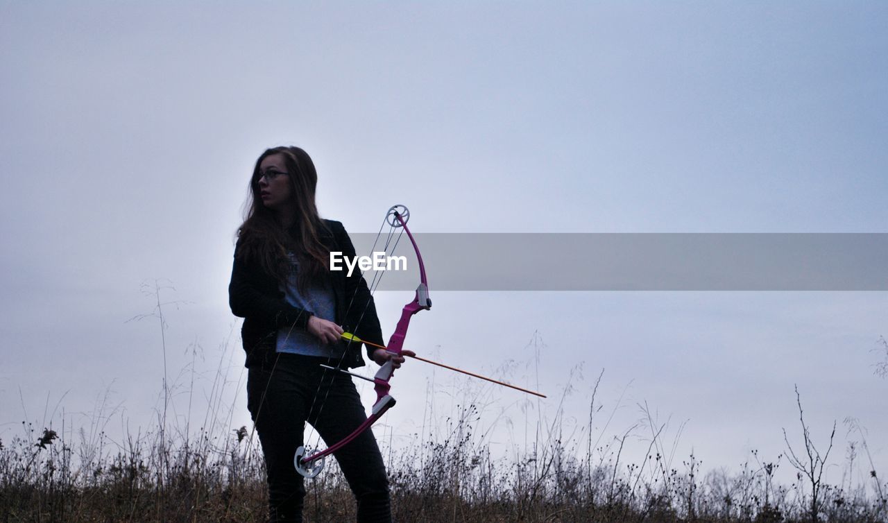 Woman practicing archery against sky