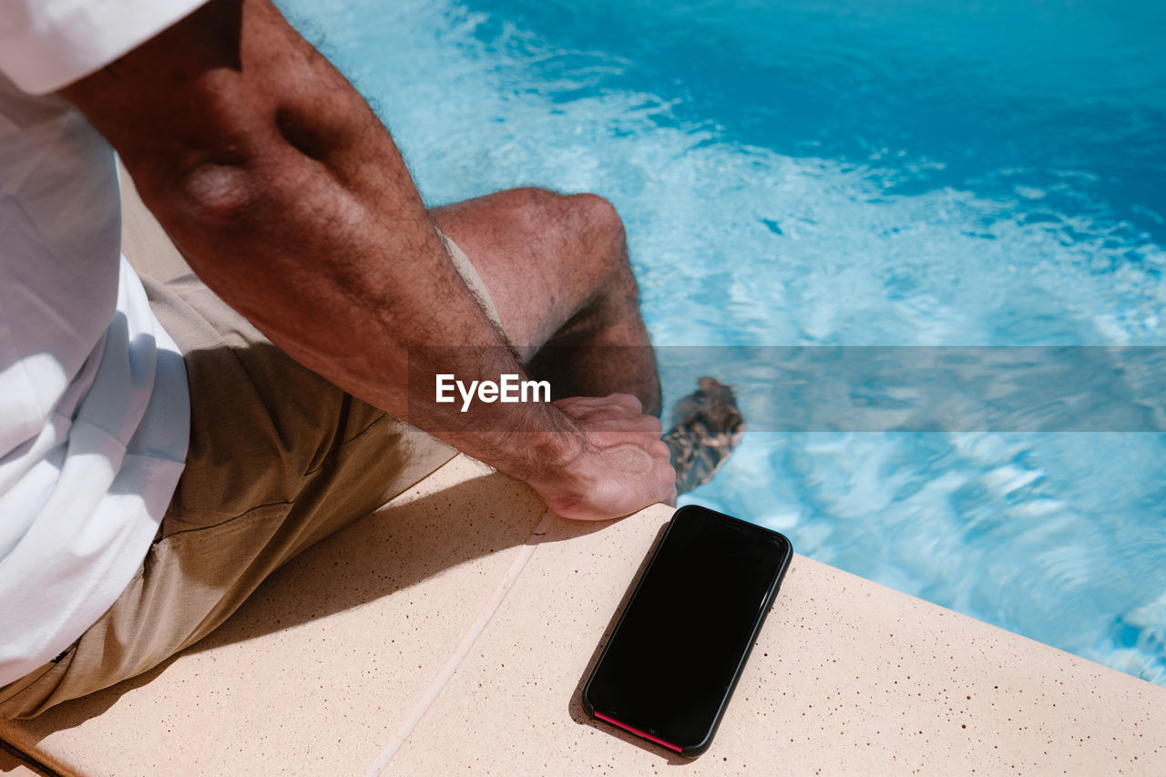 Businessman sitting poolside with mobile phone