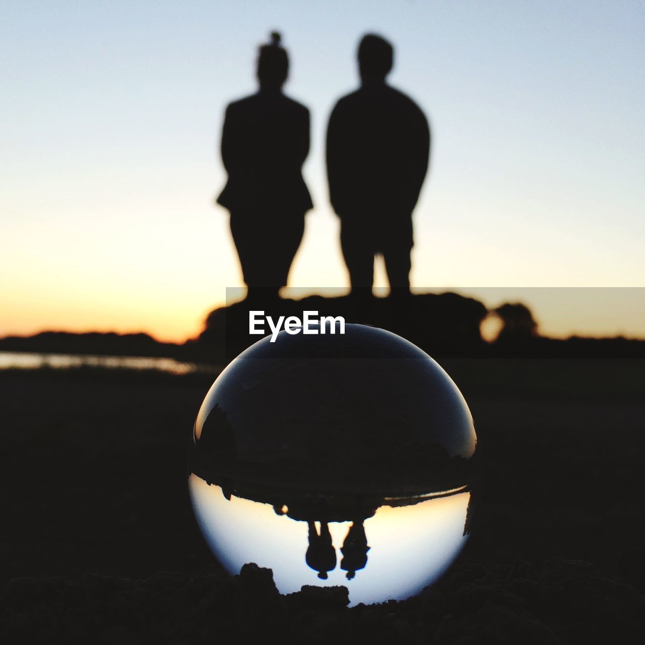 Crystal ball at beach with silhouette couple in background during sunset