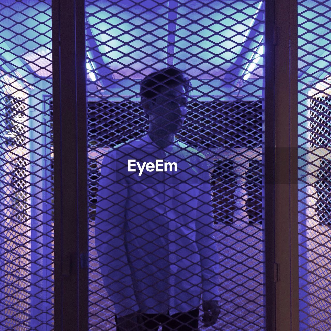 Young man seen through metal grate at night