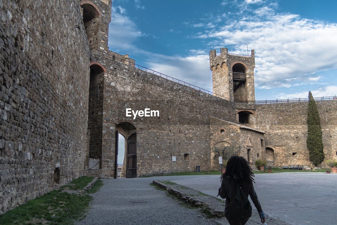 Rear view of woman walking towards historic building against sky