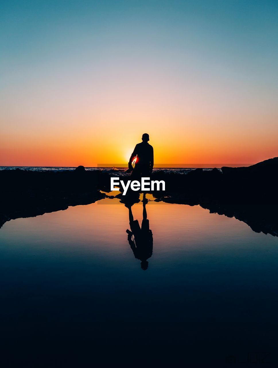 SILHOUETTE OF MAN STANDING ON LAKE