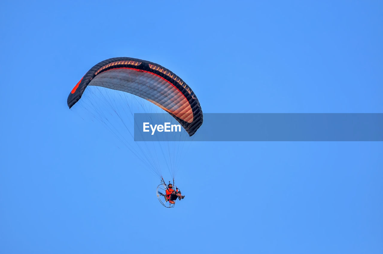 Low angle view of man paragliding against blue sky