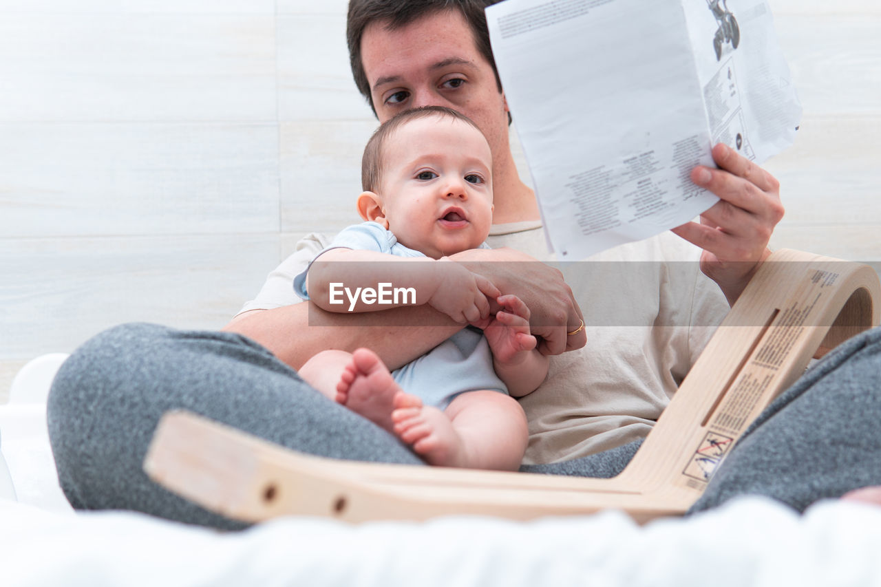 Father reading book while sitting with baby at home