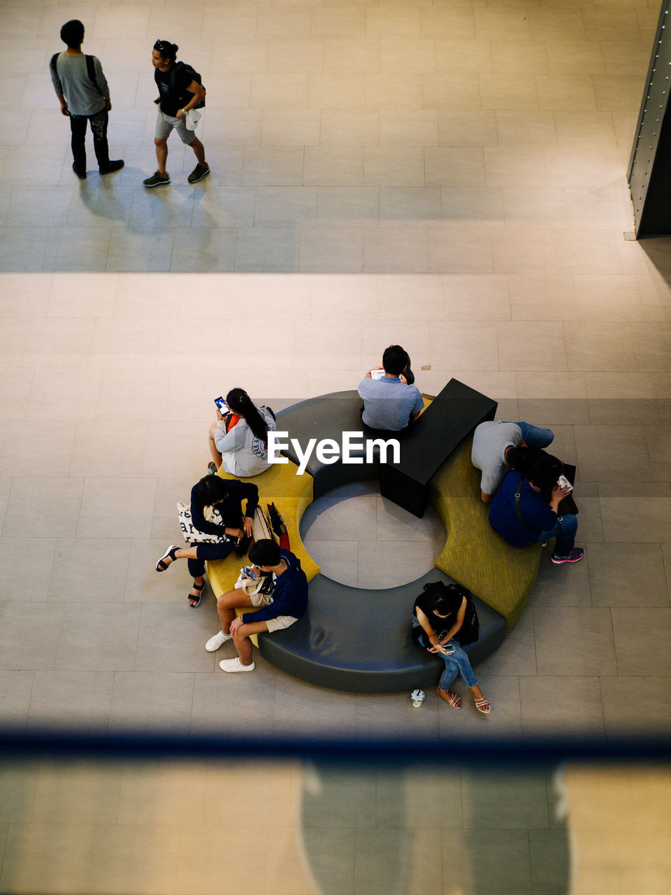 People using mobile phones while sitting on seat in city