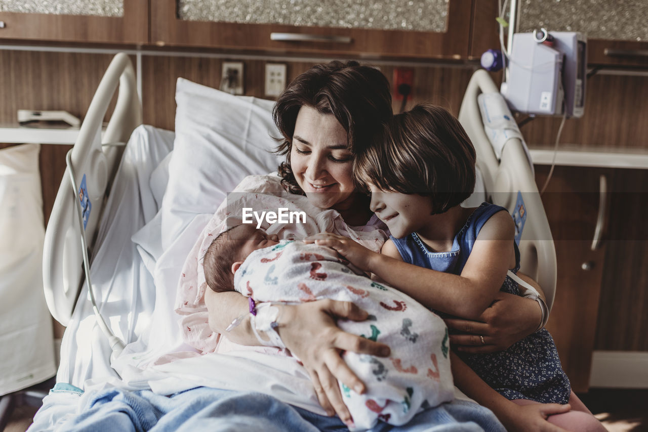 Mid view of mother holding newborn son meeting siblings