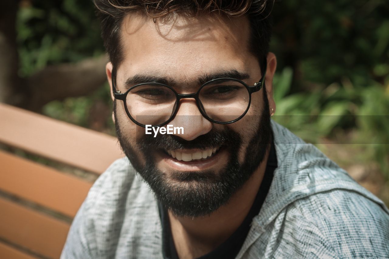 PORTRAIT OF SMILING YOUNG MAN WEARING EYEGLASSES