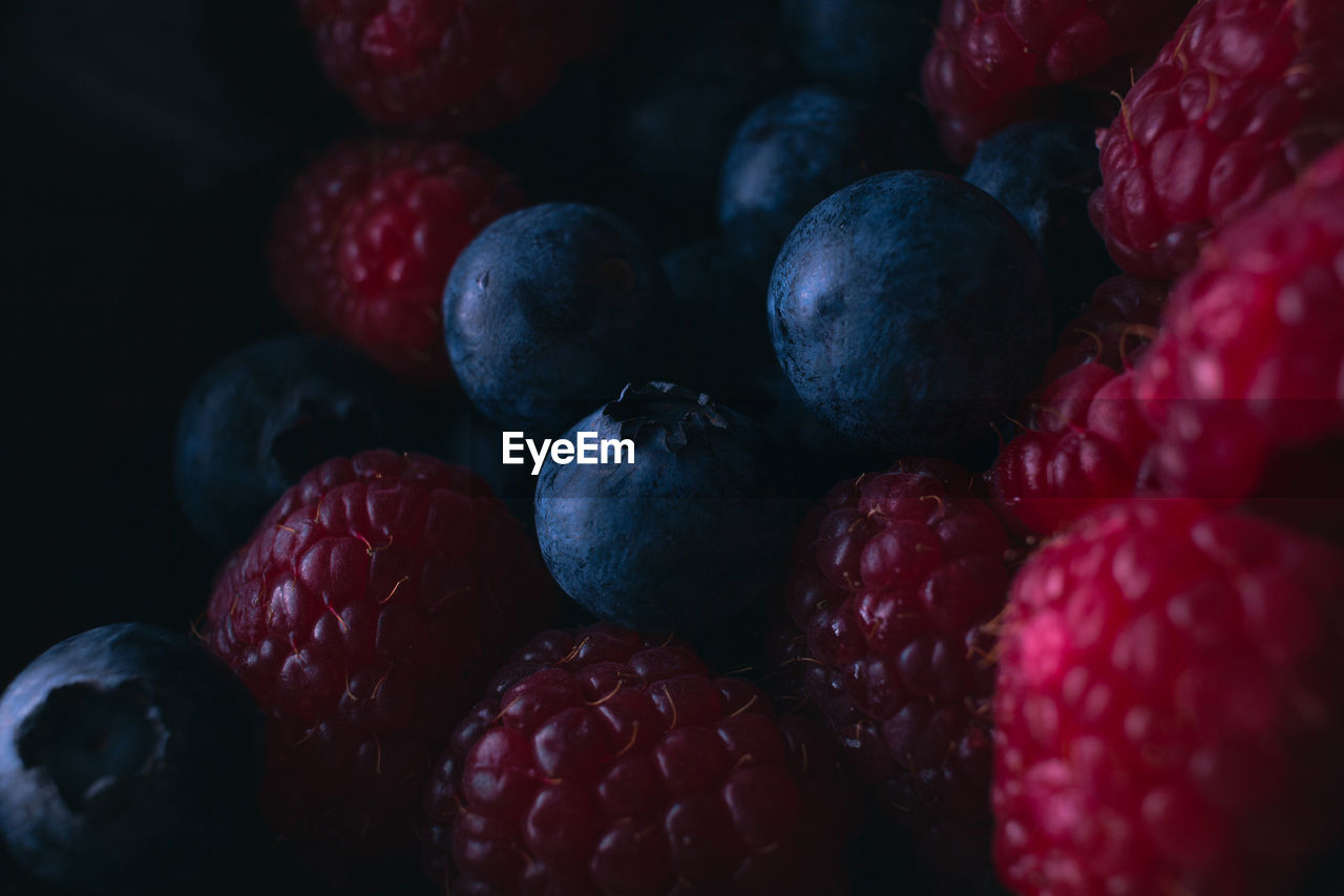 High angle view of fresh raspberries and blueberries in low light.