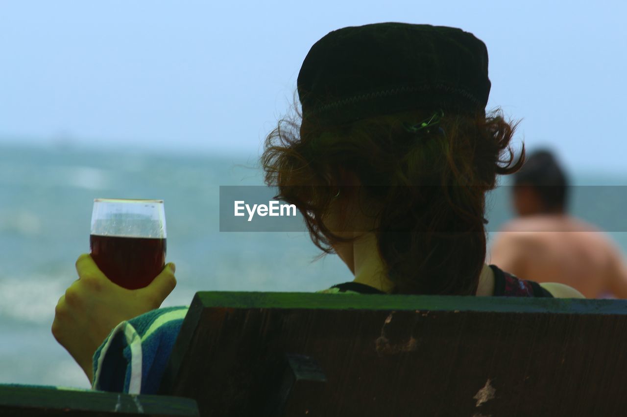 REAR VIEW OF WOMAN LOOKING AT SEA SHORE