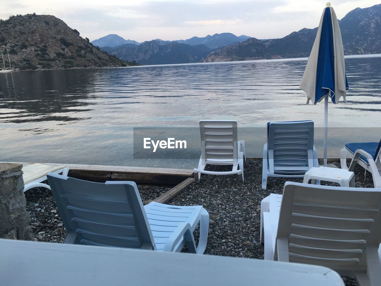 EMPTY CHAIRS AT LAKE AGAINST SKY