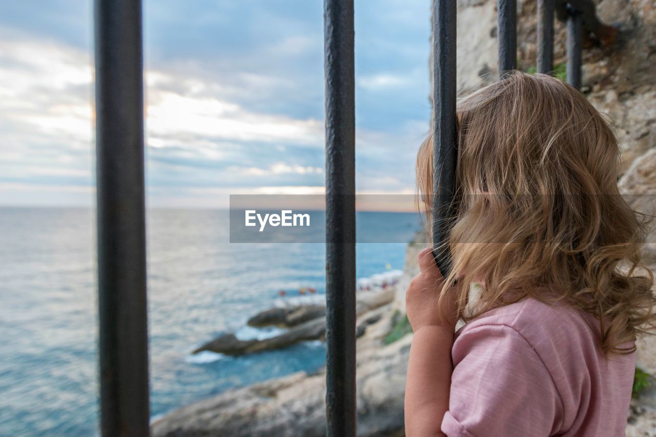 Girl looking through window at sea against sky