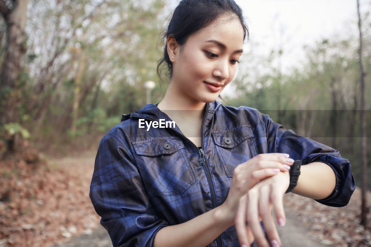 Close-up of woman checking time while standing against trees