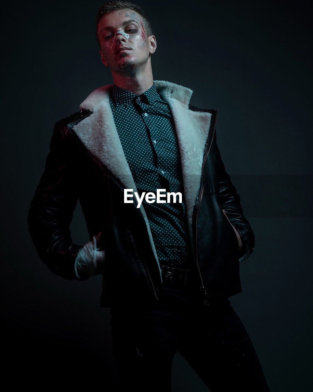 Male model wearing leather jacket while posing against black background