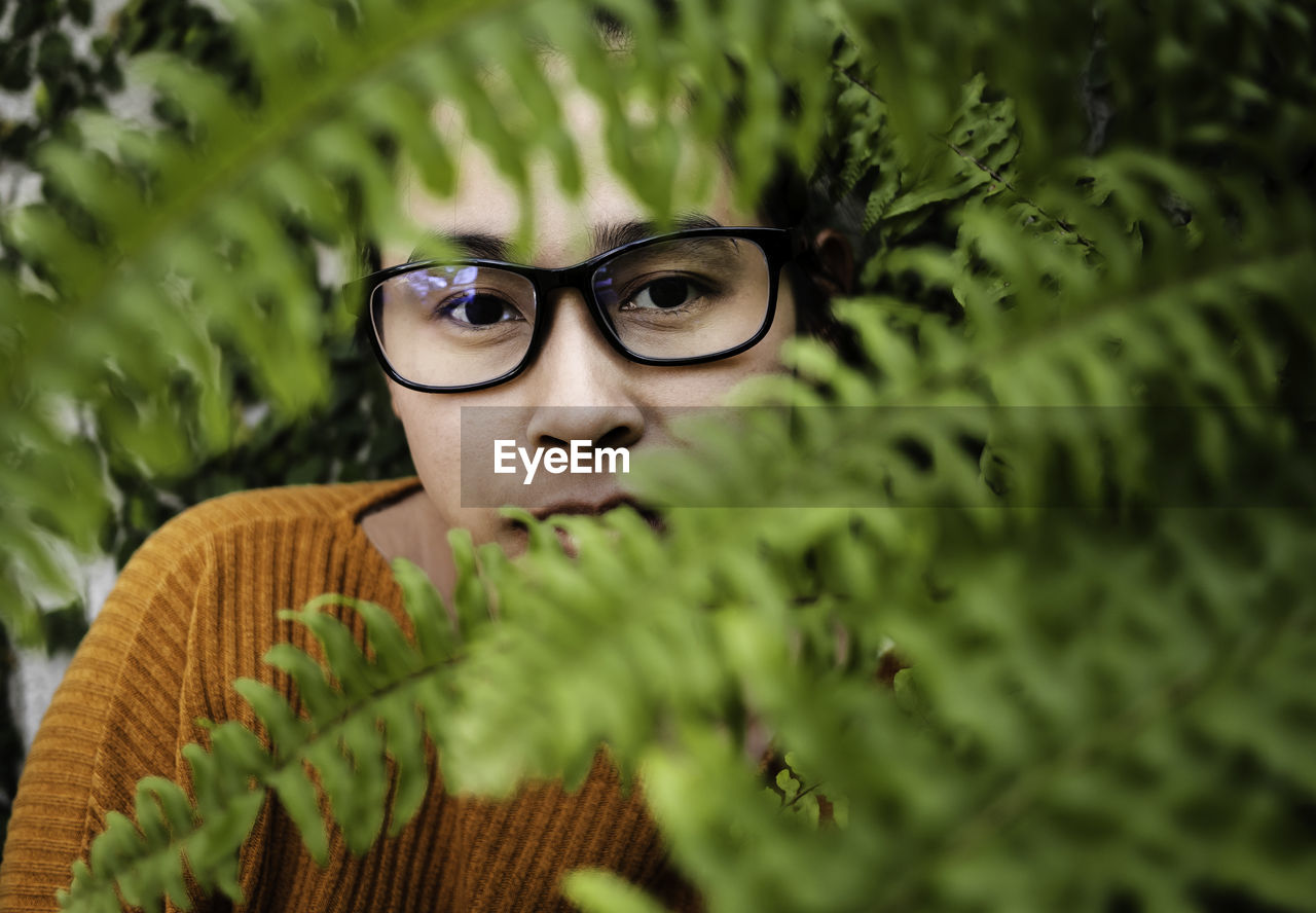 Close-up portrait of young woman wearing eyeglasses seen through leaves