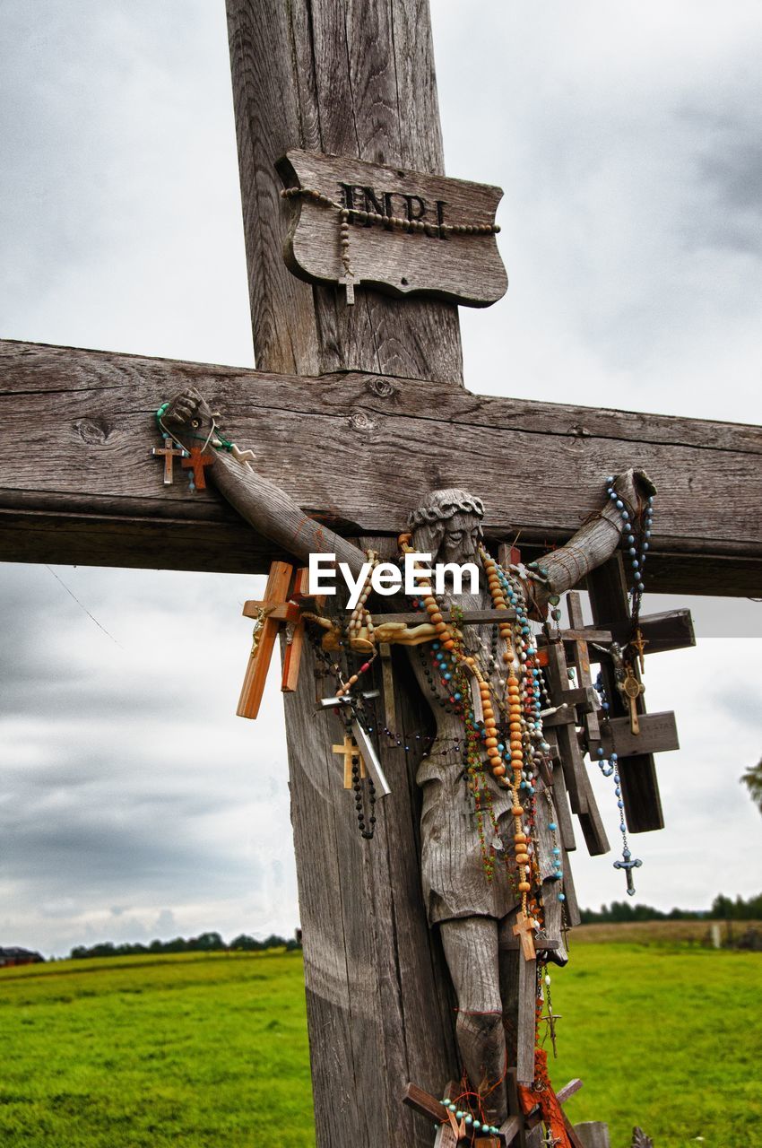 Crosses and beads hanging on wooden crucifix against sky