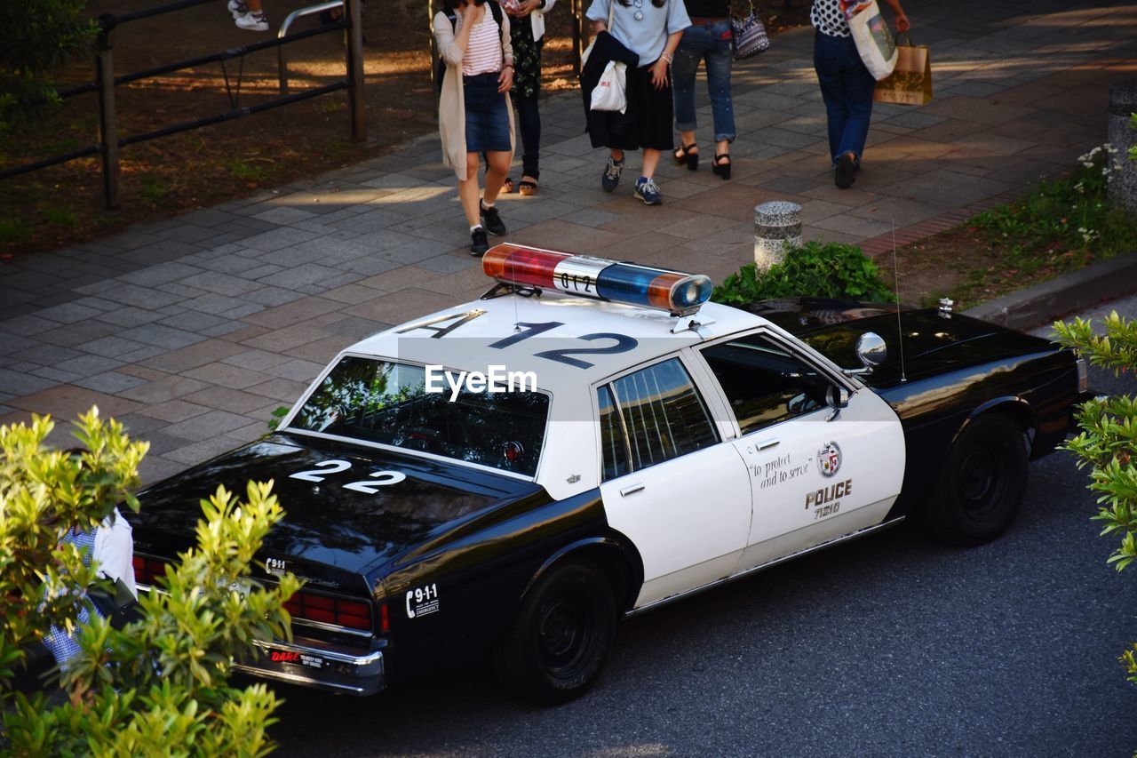 Low section of people walking by police car on street